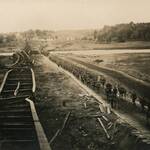 fotografia archiwalna z lotu ptaka ukazuje dywizjon piechoty uzbrojony, które idzie przy zniszczonych torach kolejowych