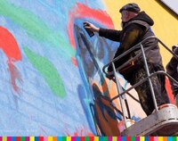 Artysta na podnośniku maluje mural sprayem na ścianie bloku
