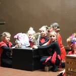 Grupa dziecięcych aktorów w czerwono-czarnych strojach na teatralnej scenie