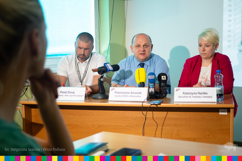 Trzej uczestnicy konferencji siedzący za stołem. W środku Przemysław Sarosiek, dyrektor białostockiego WORD. Przed nimi mikrofony mediów.
