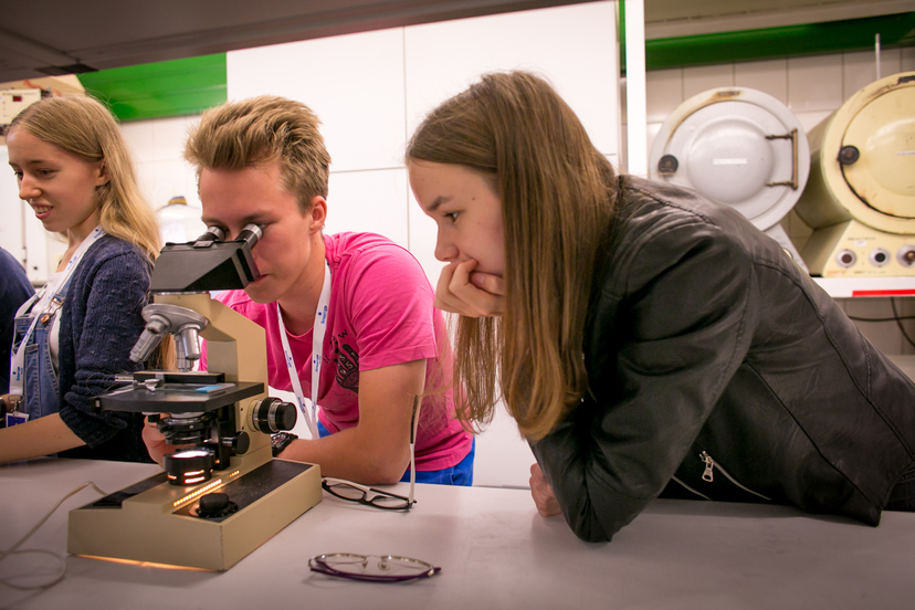 Młodzi naukowcy siedzą przy stole i oglądają preparaty pod mikroskopem - fot. Anna Liminowicz
