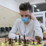 Młody chłopak w białej bluzie podpierający głowę i patrzący na szachownicę