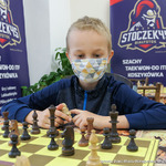 Młody szachista będący w maseczce patrzy na pole gry