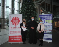 Trzy osoby stoją na tle choinki. Po lewej baner Caritasu, po prawej - Zespołu Szkół Katolickich.