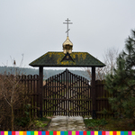 Brama uwieńczona złotą kopułą z krzyżem prawosławnym. Obok rosną drzewa i krzewy.