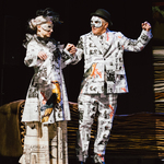 Kobieta i mężczyzna w kostiumach teatrlanych stoją trzymając się za ręce.