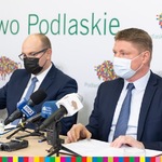 Dwóch mężczyzn siedzących przy stole na tle białego baneru z logo Województwa Podlaskiego