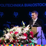 Prowadzący uroczystość na mównicy, po prawej stronie bukiet kwiatów, w tle widać logo Politechniki Białostockiej 