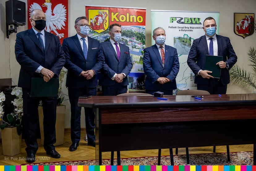 Pięciu mężczyzn, przed nimi stoi stół, za nimi widać herb Polski oraz herb miasta Kolno