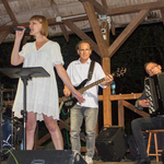 Zespół podczas występu, kobieta w białej sukience śpiewa do mikrofonu