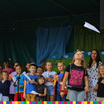 Dzieci zebrane na scenie, biorą udział w konkursie rzucania papierowymi samolotami