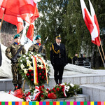 czterech mężczyzn ze służb mundurowych przed pomnikiem Obrońców Białegostoku. Po obu stronach powiewają flagi  narodowe.