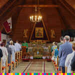 Wnętrze drewnianego kościoła. Pod ołtarzem widoczne wieńce dożynkowe. W ławkach siedzą uczestnicy wydarzenia