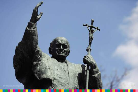 Pomnik papieża od pasa w górę. Prawa ręka uniesiona, w lewej trzyma krzyż.