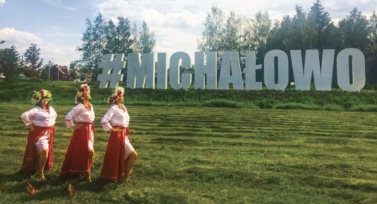 Trzy dziewczyny w strojach ludowych przed witaczem Michalowo