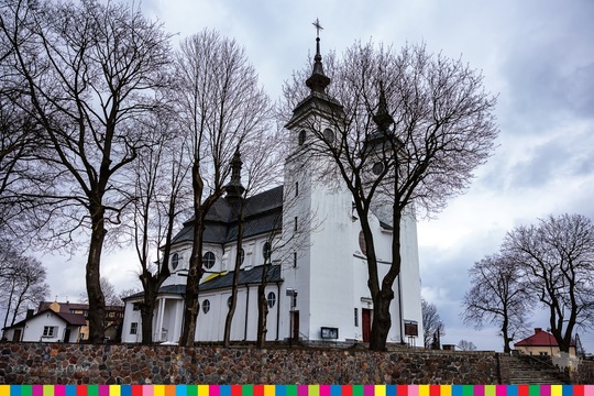 Dwuwieżowy murowany kościół w otoczeniu drzew.