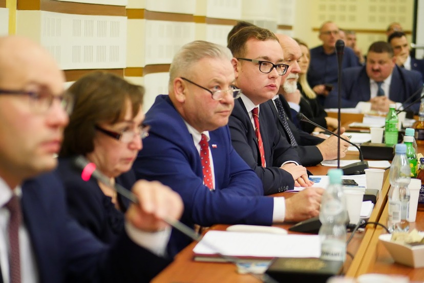 Na zdjęciu rząd osób - radnych województwa podlaskiego - przy stole do obrad. Głos zabiera pierwszy z lewej marszałek województwa Artur Kosicki