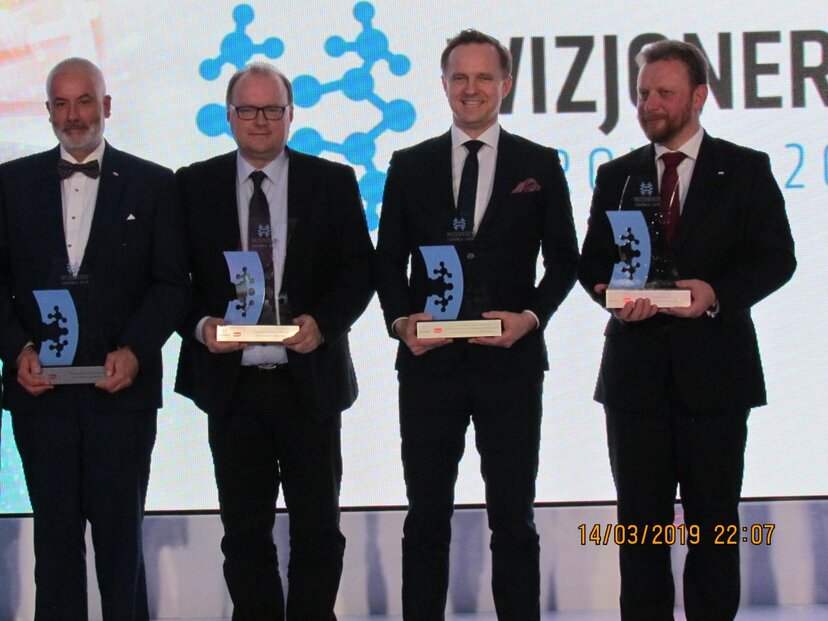 Czterech mężczyzn laureatów nagród w konkursie stoi na scenie ze statuetkami w dłoniach