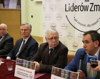 Cztery osoby - Organizatorzy Kongresu - siedzą przy stole konferencyjnym. Pierwsza osoba z prawej wypowiada się do mikrofonu