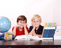 na zdjęciu dwóch uśmiechniętych chłopców siedzi przy biurku, przy otwartej książce, na biurku stoi globus, leżą mazaki i książki