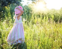 Dziewczynka w letniej sukience i kapeluszu spaceruje po łące