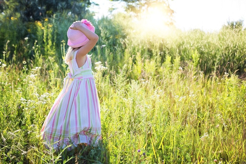 Dziewczynka w letniej sukience i kapeluszu spaceruje po łące