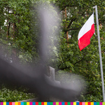 Krzyż po lewej, po prawej łopocząca na wietrze flaga Polski.