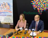 Marszałek województwa Artur Kosicki i rzeczniczka Izabela Smaczna-Jórczykowska siedzą przy stole konferencyjnym podczas briefingu. W te plakat pikniku i baner z logo województwa.