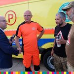 Marszałek Województwa Podlaskiego Artur Kosicki rozmawia z trzema mężczyznami, w tym ratownikiem medycznym, na tle pojazdu ratownictwa medycznego