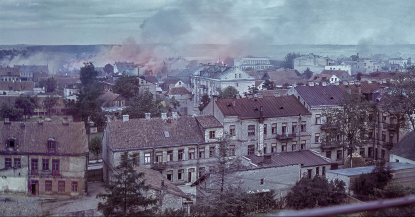 Archiwalne zdjęcie getta białostockiego z 1943 r. - ciąg kamienic z powybijanymi szybami w oknach, nad dachami unosi się dym.