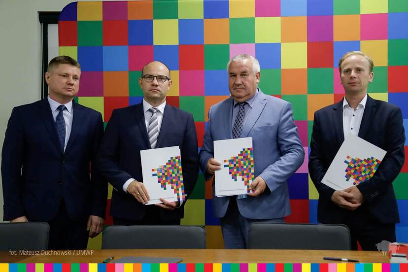 Marek Malinowski, Artur Kosicki, Kazimierz Gwiazdowski oraz Marek Sadowski stojący obok siebie prezentują podpisaną umowę na tle ścianki z logo województwa.