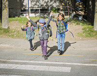 Troje dzieci z plecakami przechodzi przez jezdnię.
