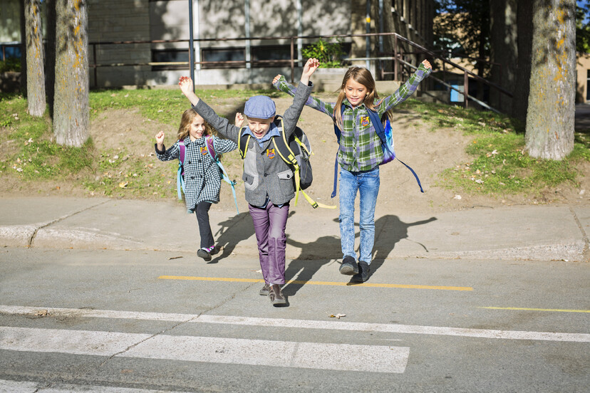 Troje dzieci z plecakami przechodzi przez jezdnię.