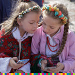 Dwie dziewczynki w strojach ludowych bawią się telefonami komórkowymi. 