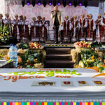 Wielki tort dożynkowy, a w tle na scenie zespół ludowy Wasiloczki z Bielska Podlaskiego. 