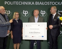 Cztery osoby prezentujące czek na ściance z logo Politechniki.