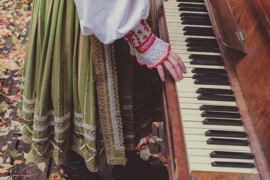 Kobieta w stroju kurpiowskim trzymająca dłonie na klawiaturze fortepianu