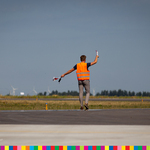 Osoba w pomarańczowej kamizelce macha lizakami, które ukierunkowują lądujące samoloty na pas startowy