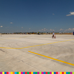 W oddali widać samoloty stojące wzdłuż pasa startowego oraz ludzi, którzy tam spacerują