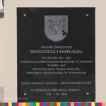 Tablica o figurach św. Benedykta i św. Romualda, które stoją przed kościołem św, Antoniego w Suwałkach, a kiedyś znajdowały się w klasztorze w Wigrach