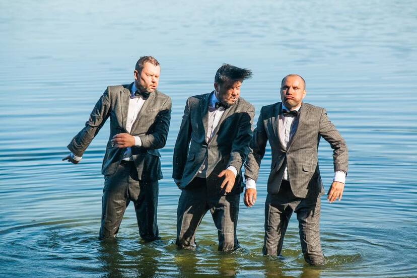Trzech mężczyzn w garniturach stojących po kolana w wodzie