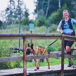 Po drewnianym moście biegnie młoda kobieta wraz z psem, którego trzyma na smyczy
