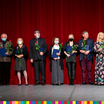 Na scenie stoją odznaczeni pracownicy teatru. W dłoniach trzymają róże. 
