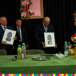 Czterech mężczyzn stoi za stołem. Dwóch, w tym marszałek Artur Kosick trzyma wycinanki ludowe.