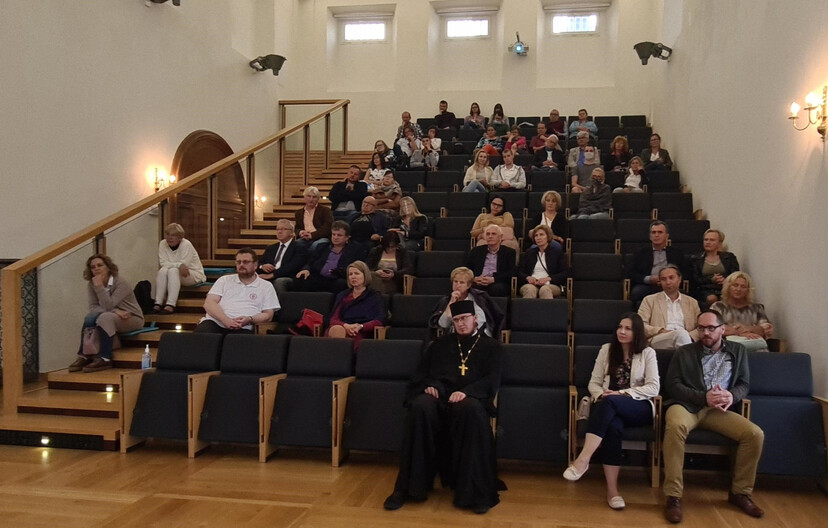 Uczestnicy spotkania siedzą na widowni. W pierwszym rzędzie duchowny prawosławny oraz kobieta i mężczyzna.