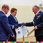 Marszałek Artur Kosicki i kobieta wręczają czek mężczyźnie w mundurze strażackim.