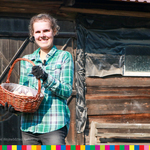 Uśmiechnięta kobieta soi przed drewnianym domem i trzyma kosz z jajami kurzymi.