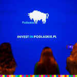 Trzy kobiety patrzą w kierunku napisu na niebieskim tle Invest in Podlaskie.pl