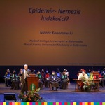Mężczyzn przemawiający z mównicy. Za nim na ekranie tytuł wykładu: Epidemie-nemezis ludzkosci?