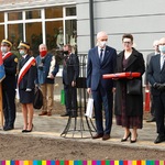 Marszałek Artur Kosicki w towarzystwie innych osób stojących przed szkołą. Z lewej strony stoi poczet sztandarowy Szkoły Weta.